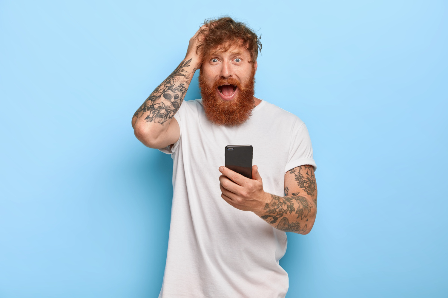 frustrated-stressful-ginger-hipster-keeps-hand-on-head-looks-with-worried-facial-expression-opens-mouth-holds-modern-cellular-feels-fear-because-of-making-mistake-did-something-wrong-with-app
